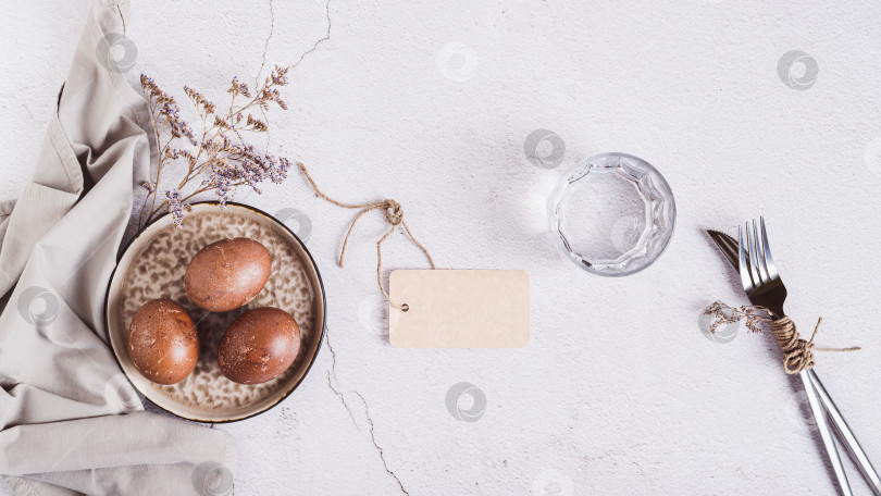 Скачать Пасхальные яйца, раскрашенные натуральным способом, на тарелке, столовые приборы и стакан воды вид сверху на веб-баннер фотосток Ozero