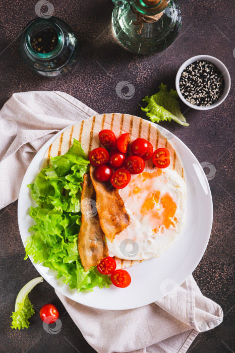 Скачать Тако на гриле с яйцом, жареным беконом, овощами и зеленью на тарелке в вертикальном положении фотосток Ozero