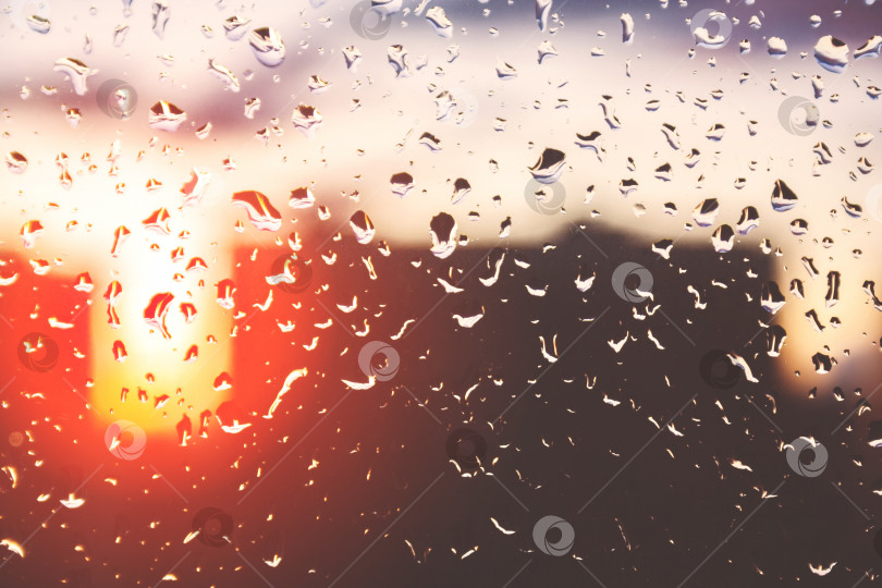 Скачать Капли дождя на оконном стекле на фоне заката или восхода солнца и городских домов (тонированные, концептуальные) фотосток Ozero