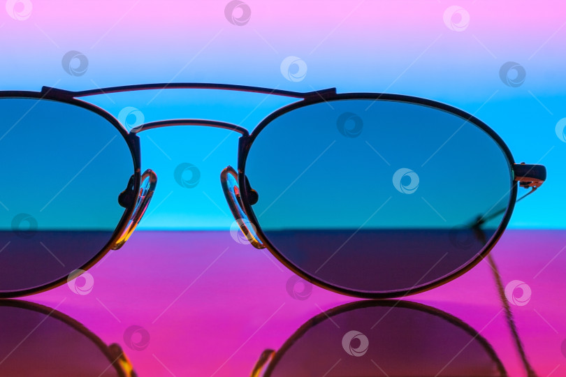 Скачать Крупный план солнцезащитных очков на зеркальной поверхности на цветном градиентном фоне фотосток Ozero