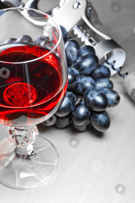 Скачать Крупный план бокала красного вина рядом с гроздью черного винограда и пробкой со штопором на деревянном столе (концепция, цветовой акцент, небольшая глубина резкости) фотосток Ozero