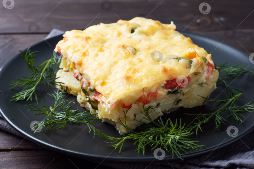 Скачать Запеканка из картофеля и овощей с сыром на тарелке. Фон из темного дерева. Сомкнуться фотосток Ozero