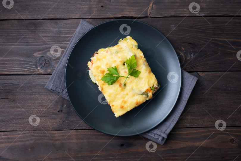 Скачать Запеканка из картофеля и овощей с сыром на тарелке. Фон из темного дерева. Скопируйте пробел. фотосток Ozero