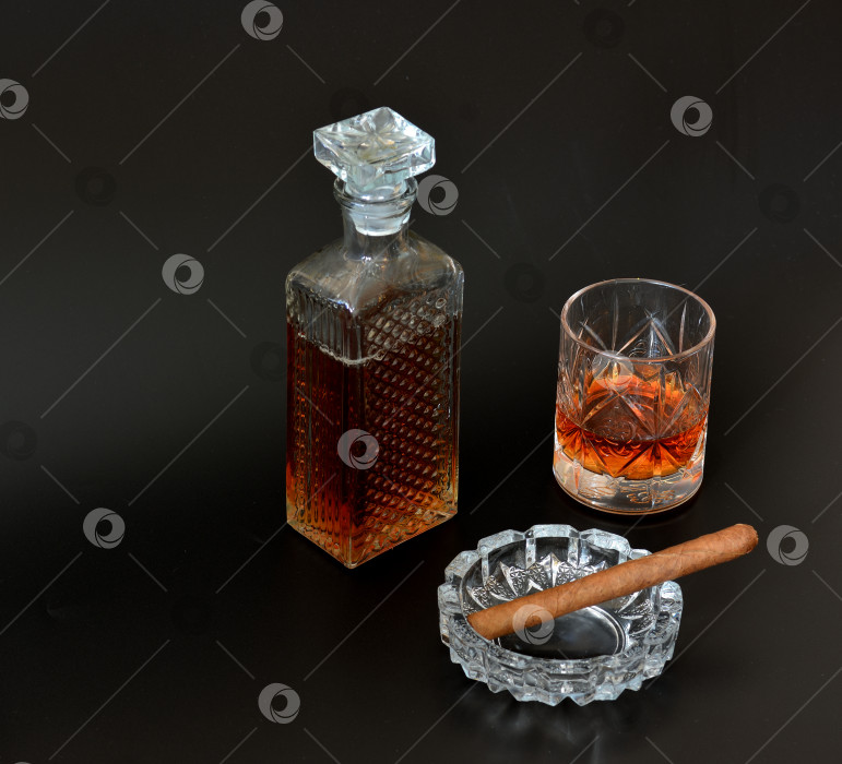 Скачать Стеклянная пепельница с сигарой, хрустальный графин и бокал виски на черном фоне. фотосток Ozero