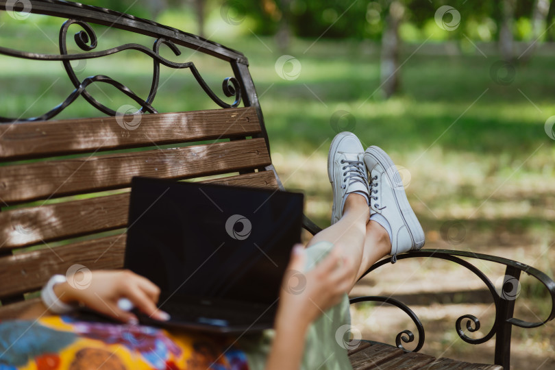 Скачать Женщина работает за своим ноутбуком, лежа на скамейке в парке, фото без лица фотосток Ozero