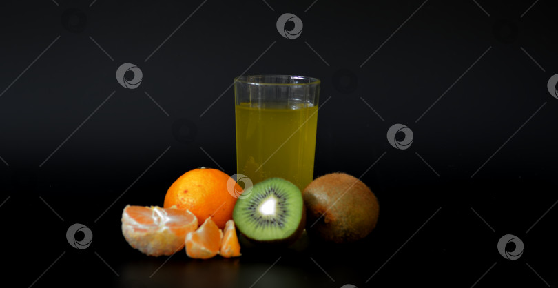 Скачать Бокал со смесью тропических фруктов с косточками на черном фоне, рядом со спелым мандарином и киви. фотосток Ozero
