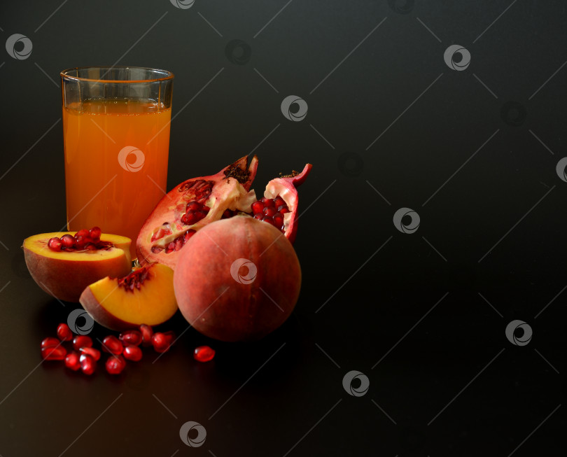 Скачать Смесь фруктовых соков в высоком стакане на черном фоне с кусочками спелого персика и разломанного граната. фотосток Ozero