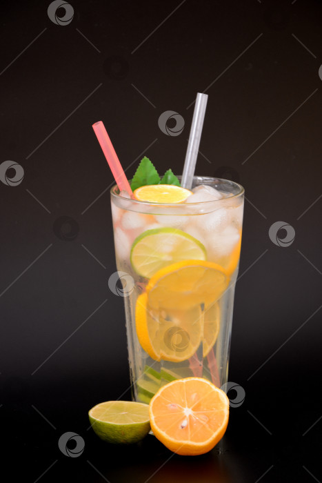 Скачать Высокий граненый стакан освежающего лимонада со льдом на черном фоне, рядом с кусочками спелого апельсина и лайма. фотосток Ozero