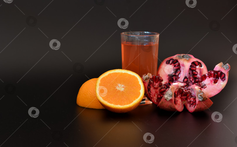 Скачать Стакан свежего фруктового сока на черном фоне и кусочки апельсина и спелого граната рядом. фотосток Ozero