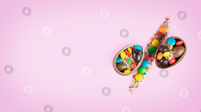 Скачать Половинки шоколадных пасхальных яиц и разноцветных конфет в виде знака процента на розовом фоне. Концепция рекламы праздничных распродаж. Место для текста фотосток Ozero