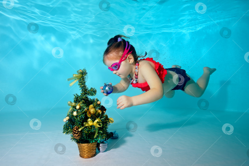 Скачать Ребенок под водой в детском бассейне украшает новогоднюю елку рождественскими игрушками. Портрет. Съемка под водой. фотосток Ozero
