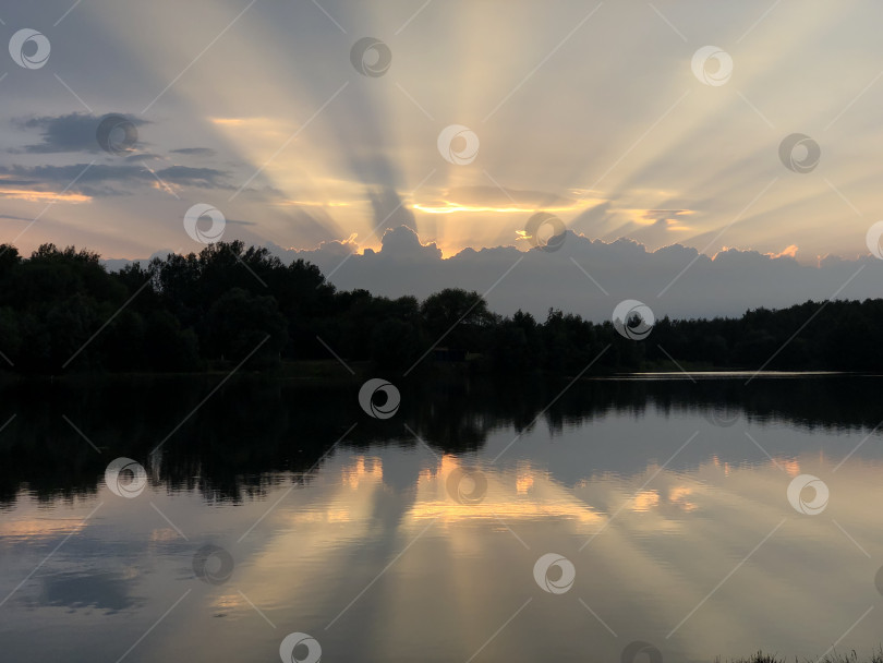 Скачать солнечные лучи в виде короны пробиваются из-за большого облака на вечернем небе и отражаются на спокойной водной глади озера фотосток Ozero