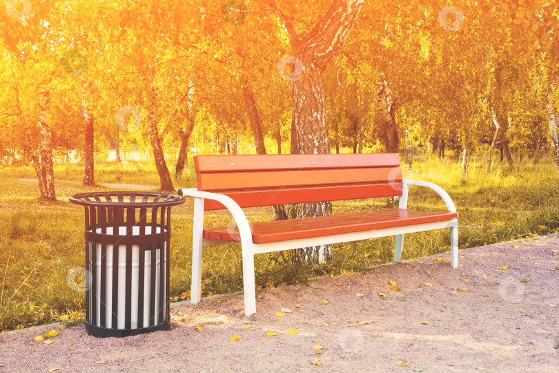 Скачать Деревянная скамейка и металлический мусорный бак в парке на фоне зеленых деревьев и заката (тонированный) фотосток Ozero