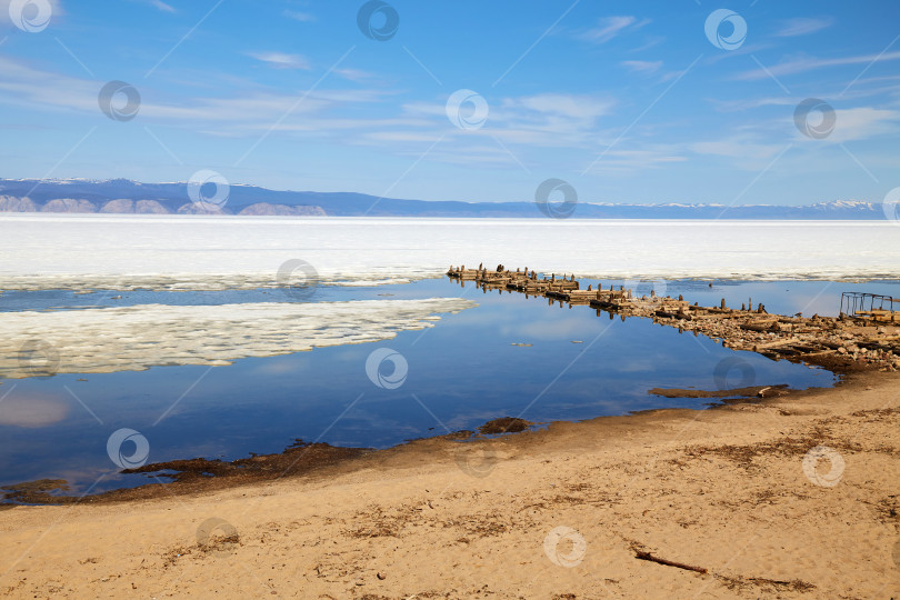 Скачать Песчаный пляж, старый разрушенный деревянный причал на острове Ольхон весной. Озеро Байкал во время ледохода. фотосток Ozero