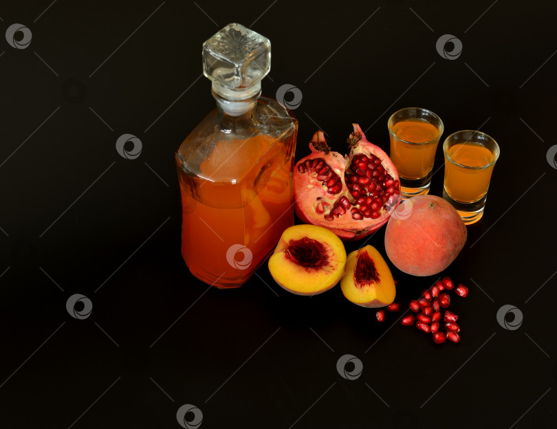Скачать Домашний фруктовый ликер в бутылке и два бокала на черном фоне, рядом с кусочками спелого персика и разломанным плодом граната. фотосток Ozero