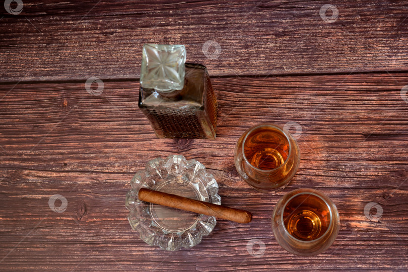 Скачать Хрустальный графин, два бокала с коньяком и хрустальная пепельница с кубинской сигарой на столе из темного дерева. фотосток Ozero