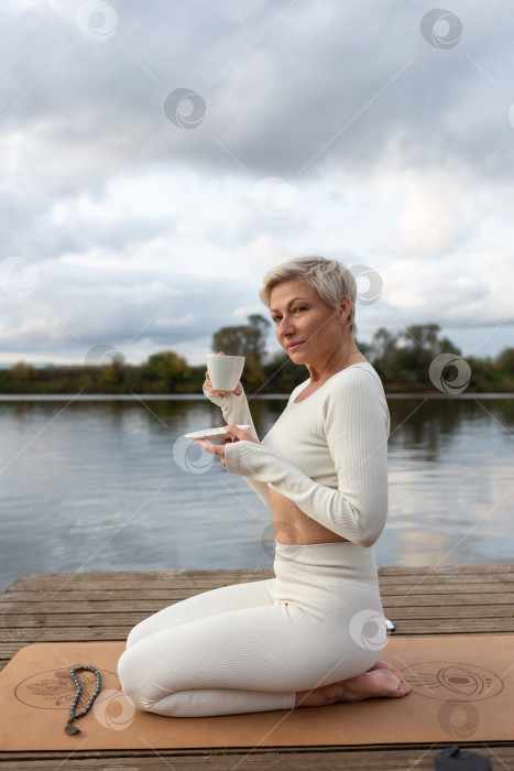 Скачать Портрет взрослой стройной женщины, пьющей чай после занятий йогой на открытом воздухе фотосток Ozero