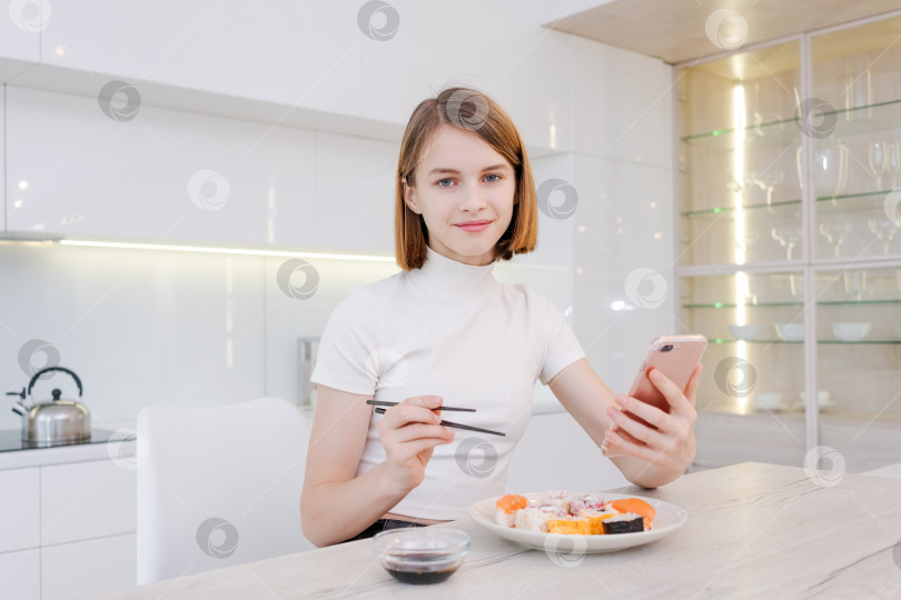 Скачать женщина ест суши и смотрит в свой телефон фотосток Ozero