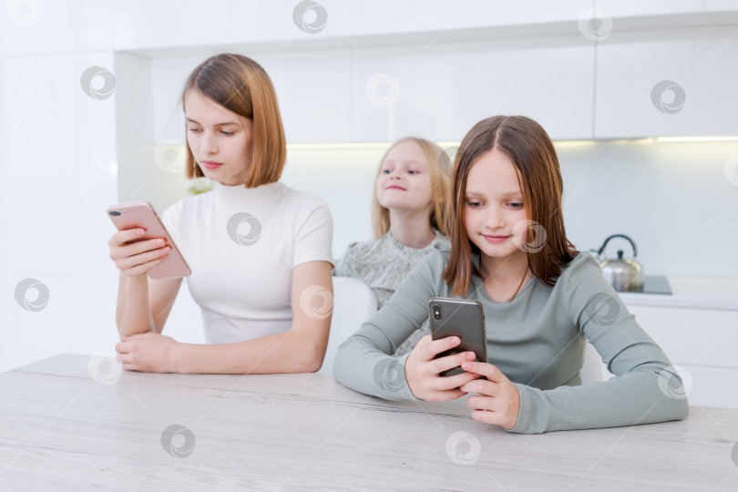 Скачать За столом сидят три девушки, каждая смотрит в свои мобильные телефоны фотосток Ozero