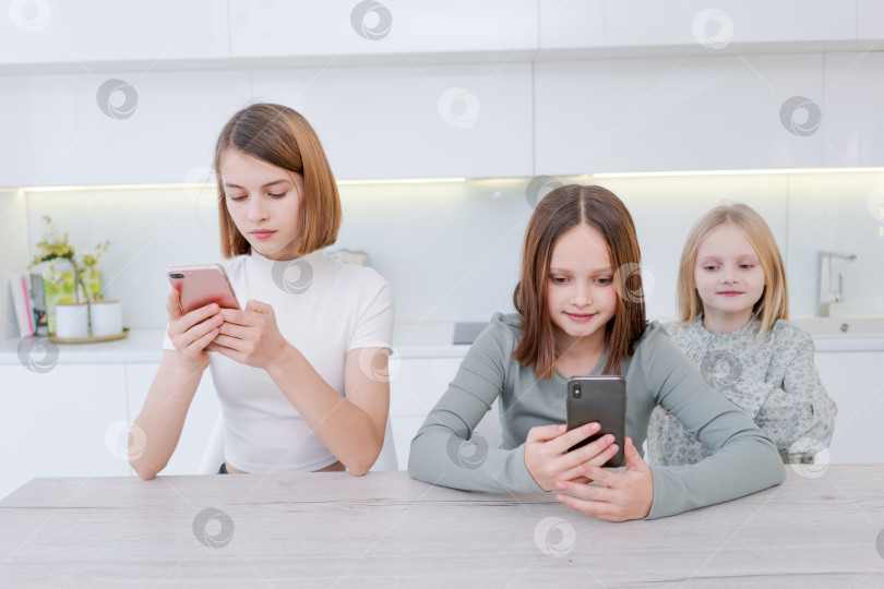 Скачать За столом сидят три девушки, каждая смотрит в свои мобильные телефоны фотосток Ozero