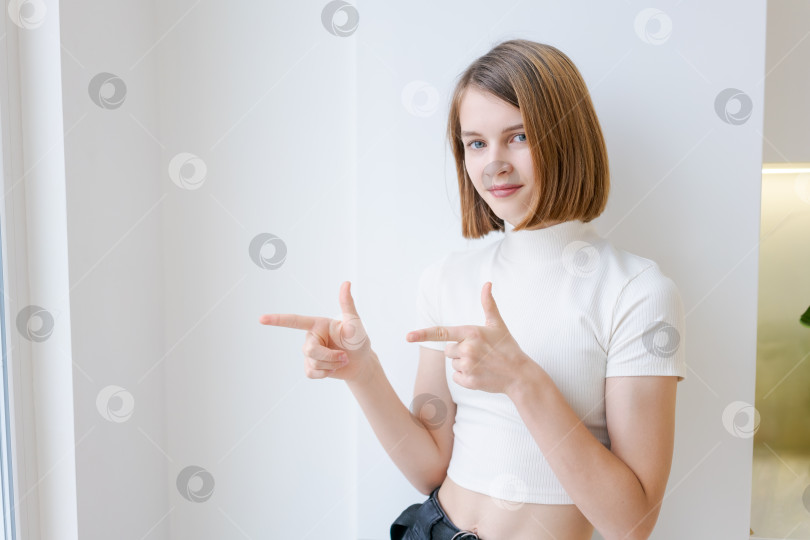 Скачать Молодая женщина стоит перед белой стеной и указывает направо фотосток Ozero