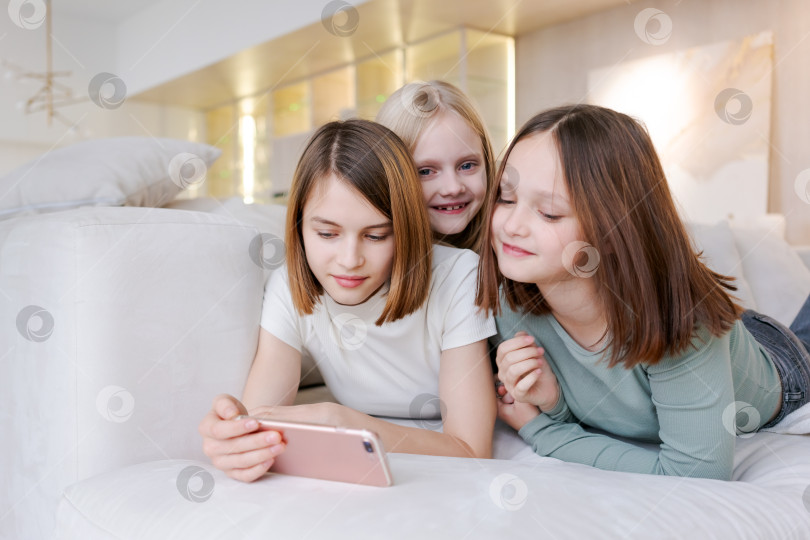 Скачать Три девушки лежат на диване и смотрят в телефон фотосток Ozero