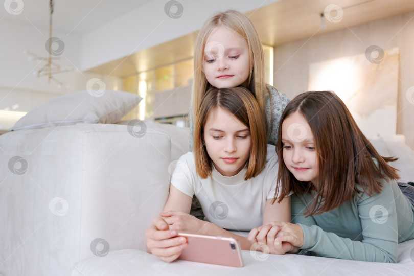 Скачать Три девушки лежат на диване и смотрят в телефон фотосток Ozero