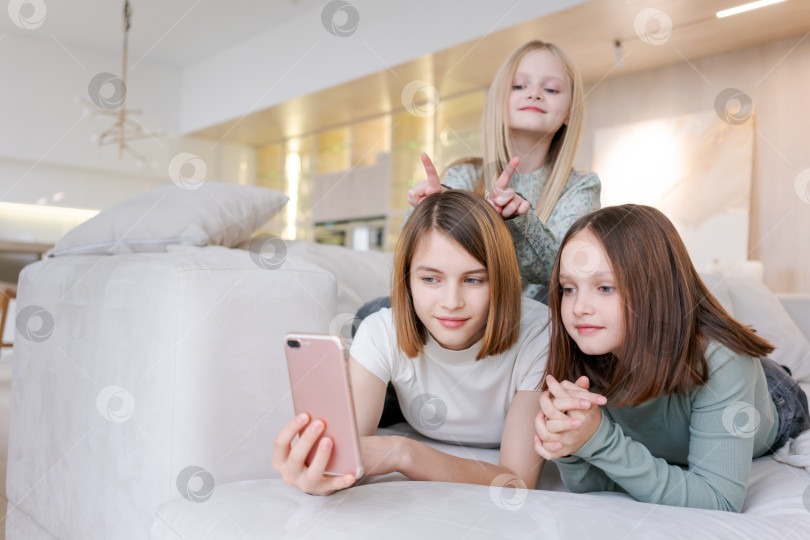 Скачать Три девушки лежат на диване, у одной из них в руках сотовый телефон фотосток Ozero
