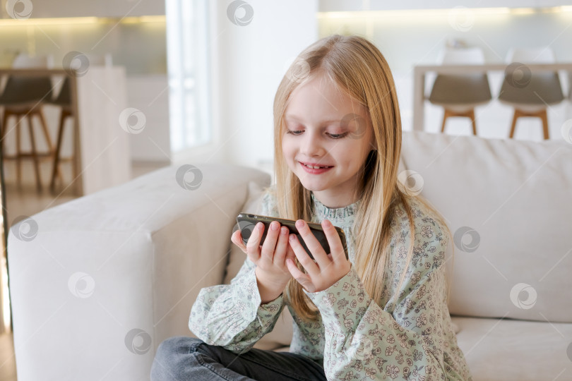 Скачать Молодая девушка сидит на диване и играет в видеоигру на своем телефоне фотосток Ozero