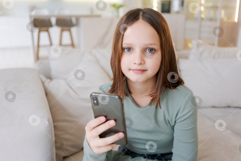 Скачать Молодая девушка сидит на диване, держа в руках сотовый телефон фотосток Ozero
