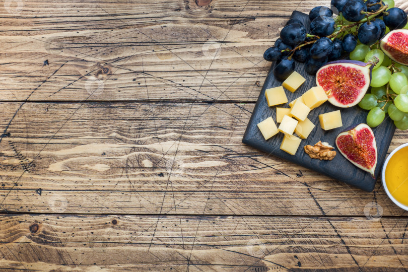 Скачать Кубики сыра, свежие фрукты - инжир, виноград, мед, грецкий орех - разложите на деревянной разделочной доске. Выделите место. фотосток Ozero