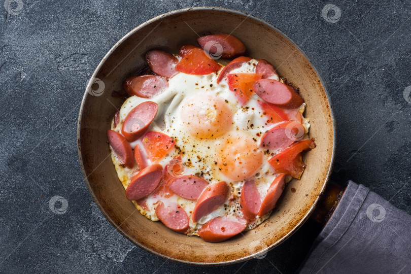 Скачать На столе сковорода с яичницей, сосисками и помидорами. Сытный домашний завтрак. фотосток Ozero