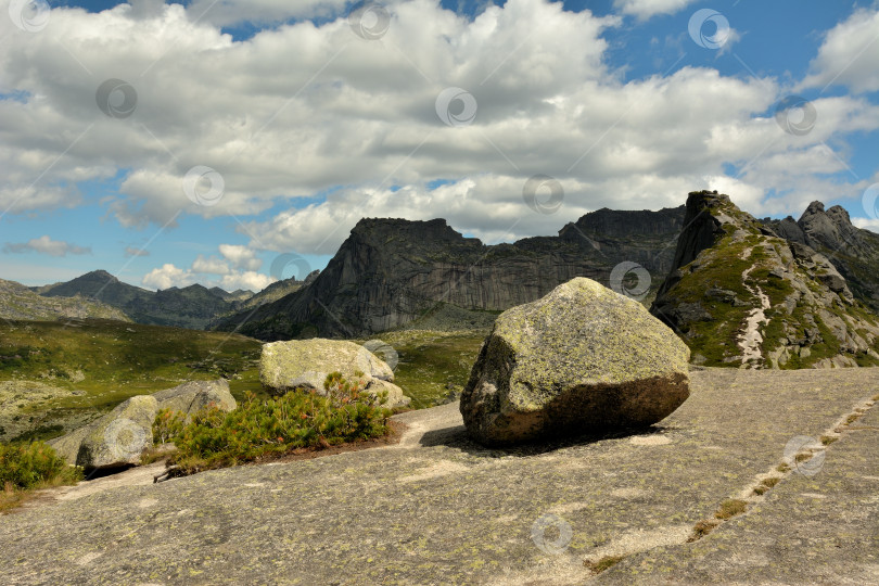 Скачать Большие камни на вершине огромной гранитной природной плиты с видом на живописные горы на фоне летнего облачного неба. фотосток Ozero
