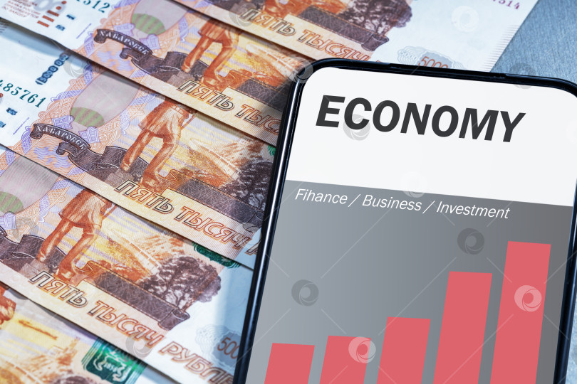 Скачать Мобильный телефон с финансовым графиком роста экономики России и рублевыми банкнотами. фотосток Ozero