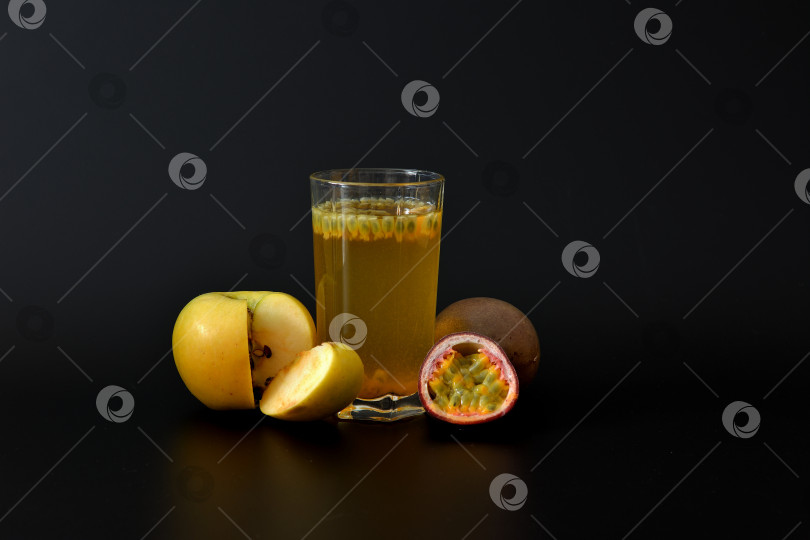 Скачать Стакан фруктового сока на черном фоне с семенами и ломтиками спелого зеленого яблока и нарезанной маракуйи. фотосток Ozero
