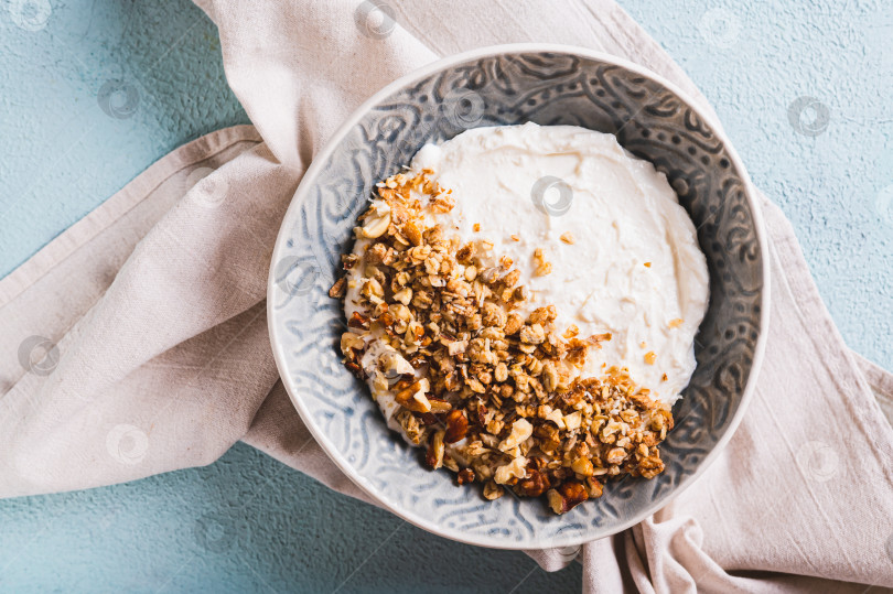 Скачать Тарелка с йогуртом, мюсли и орехами для полезного завтрака крупным планом на столе, вид сверху фотосток Ozero