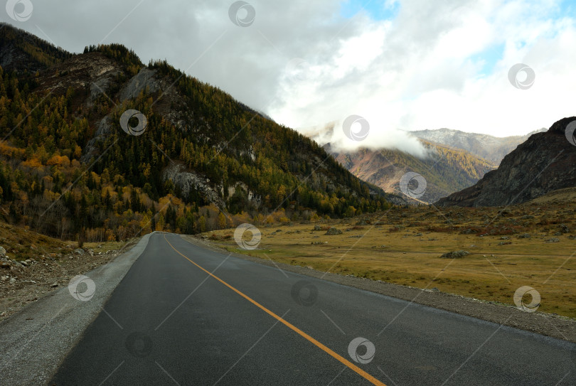 Скачать Пасмурным осенним днем новая асфальтированная дорога пересекает долину с расщелиной в горах. фотосток Ozero