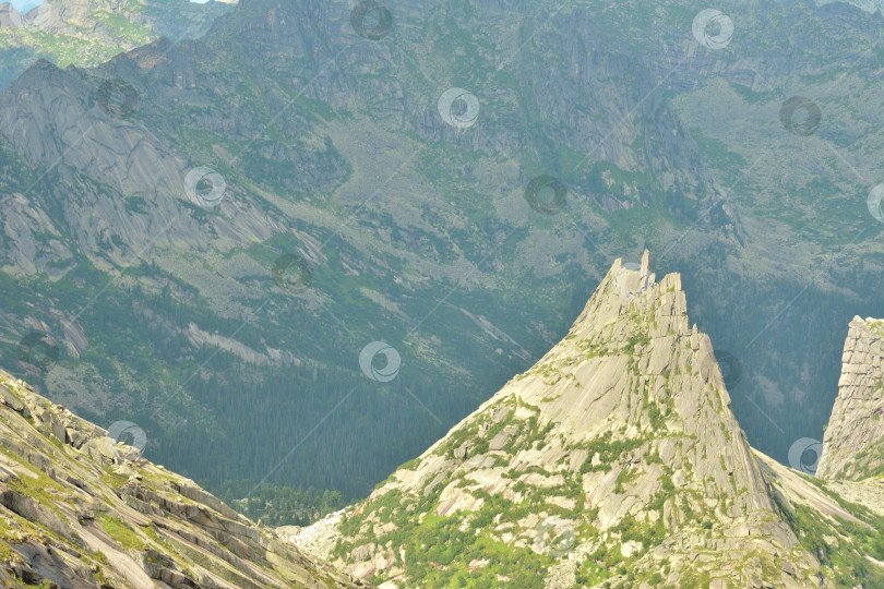 Скачать Высокая отвесная скала с остроконечной вершиной, окруженная высокими горами в солнечный летний день. фотосток Ozero