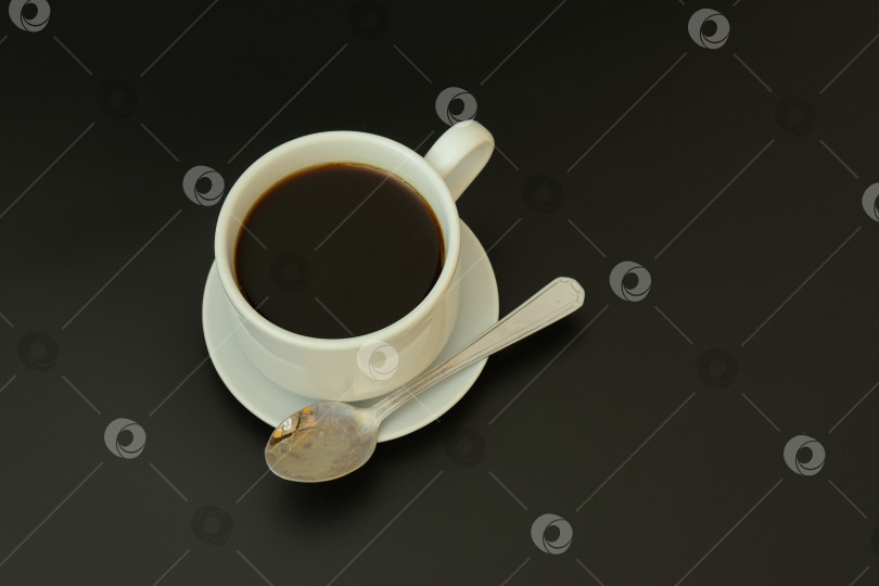 Скачать Белая керамическая чашка черного кофе на блюдце с маленькой ложечкой на черном фоне. фотосток Ozero