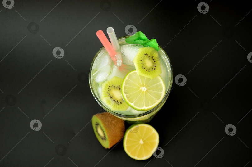 Скачать Высокий стакан освежающего фруктового сока со льдом на черном фоне, рядом с ломтиками лайма и спелым киви. фотосток Ozero
