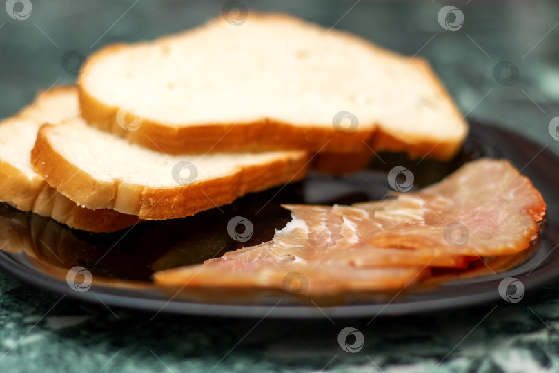 Скачать Такие пищевые ингредиенты, как ломтики мяса и хлеба, подаются на черной тарелке фотосток Ozero