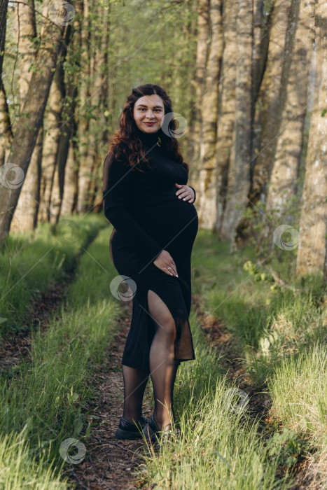 Скачать Портрет счастливой и гордой беременной женщины, смотрящей в камеру в парке на закате с теплым задним светом на заднем плане. фотосток Ozero