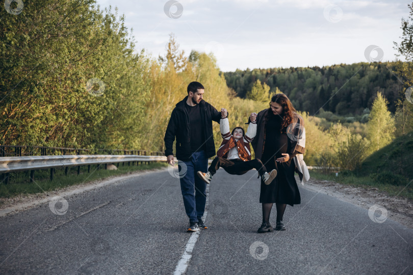 Скачать Портрет семьи с ребенком, гуляющей в парке. Мама и папа, взявшись за руки, играют с сыном и раскачивают его. фотосток Ozero