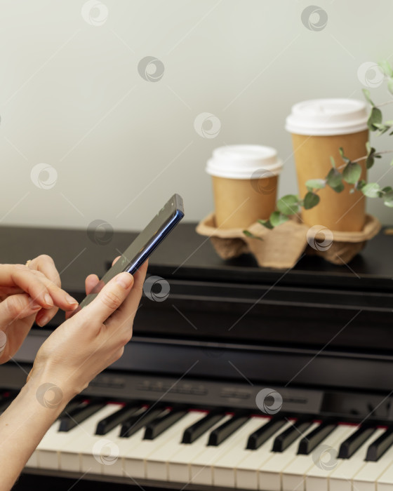 Скачать Женские руки держат смартфон перед пианино с двумя чашками кофе фотосток Ozero