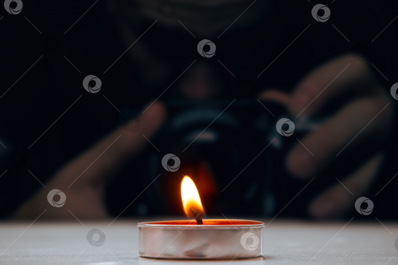 Скачать Горящая свеча, стоящая на столе, на заднем плане мужчина, фотографирующий пламя. Мягкий селективный селективный фокус фотосток Ozero