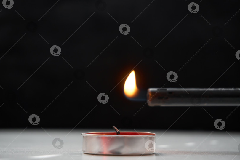 Скачать Зажигалка зажигает свечу, стоящую на плоском столе, черный фон, много свободного пространства. Избирательный избирательный фокус фотосток Ozero