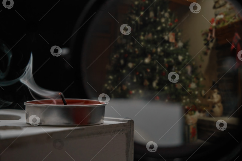 Скачать Дымящаяся свеча стоит на деревянном ящике, на обратной стороне на темном фоне расположены зеркала, в которых отражаются рождественская елка и игрушки. Избирательный фокус фотосток Ozero