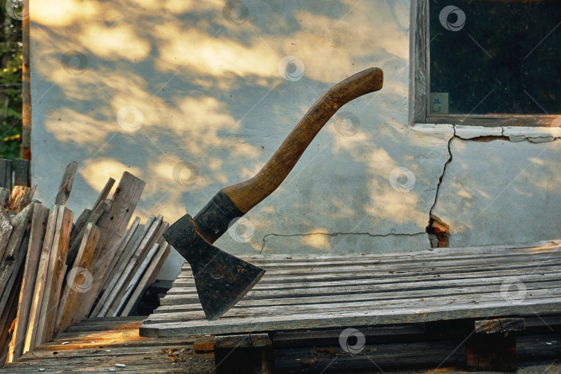 Скачать Плотницкий инструмент плотника - это двуручный топор с широким лезвием. Топор торчит из доски на фоне потрескавшейся стены - выборочный трюк фотосток Ozero