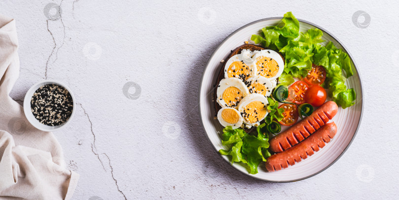 Скачать Тарелка с сосисками, бутербродом с яйцом, помидорами и листьями салата на столешнице посмотреть веб-баннер фотосток Ozero