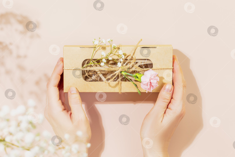 Скачать Женские руки держат подарочную коробку ручной работы с нежными цветами на розовом фоне фотосток Ozero